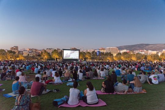 An open-air cinema in Athens at dusk, with the city behind the screen