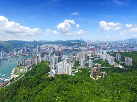 Aerial view of Tsuen Wan's high-rise towers along the Rambler Channel, with green hills and the container port in the distance