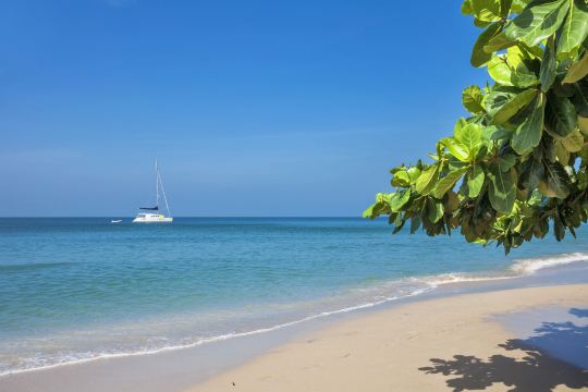 A white sailboat anchored off a quiet Phuket beach under a clear sky