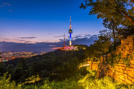 The N Seoul Tower on Namsan at dusk, above the wooded slopes and the old city wall