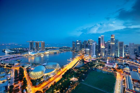 Singapore at dusk from above, with Marina Bay Sands, the CBD towers, and the river mouth lit along the waterfront
