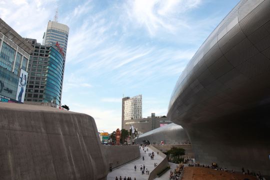 The curved metal walls of the Dongdaemun Design Plaza in Seoul, with people walking down the plaza ramp