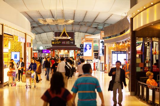 The departures hall inside Suvarnabhumi Airport, with passengers and shops under the terminal roof