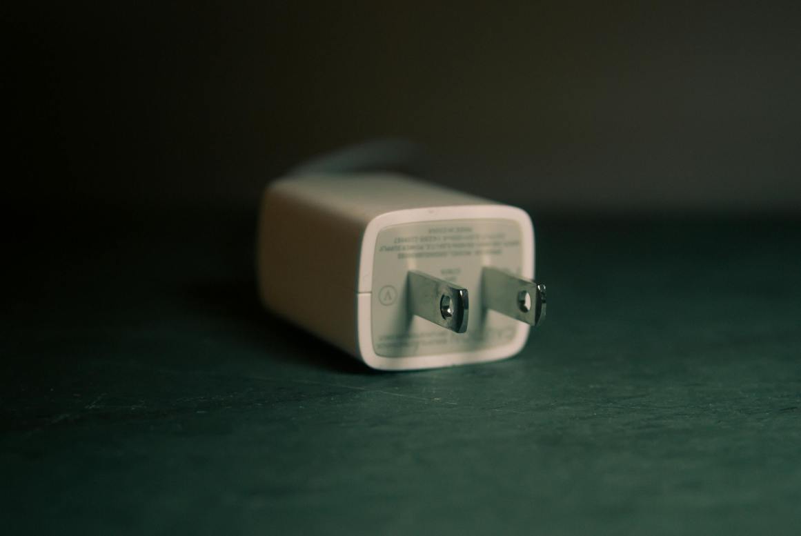 A focused view of a white wall charger plug lying on its side indoors. Via Pexels (by Steve A Johnson)