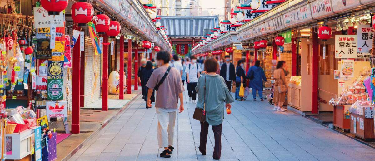 Calle comercial tradicional de Japón con faroles rojos y turistas caminando entre tiendas de recuerdos.