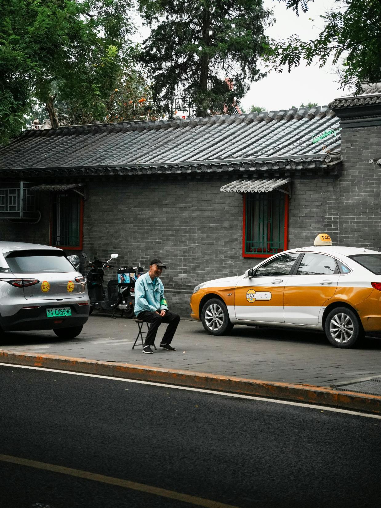 Seorang pria duduk di dekat taksi di jalan tradisional Beijing, memperlihatkan kehidupan perkotaan. Via Pexels (by Da Na)