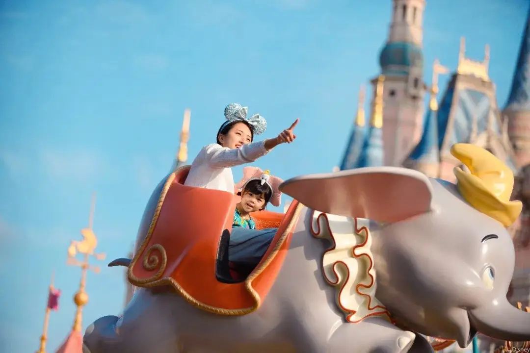 上海ディズニーランドのダンボ・ザ・フライング・エレファントに乗る親子。後方にはお城が見える。