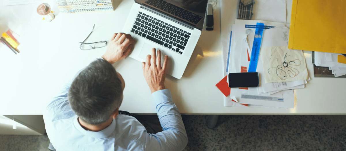 Hombre trabajando con portátil en escritorio con documentos y objetos de oficina