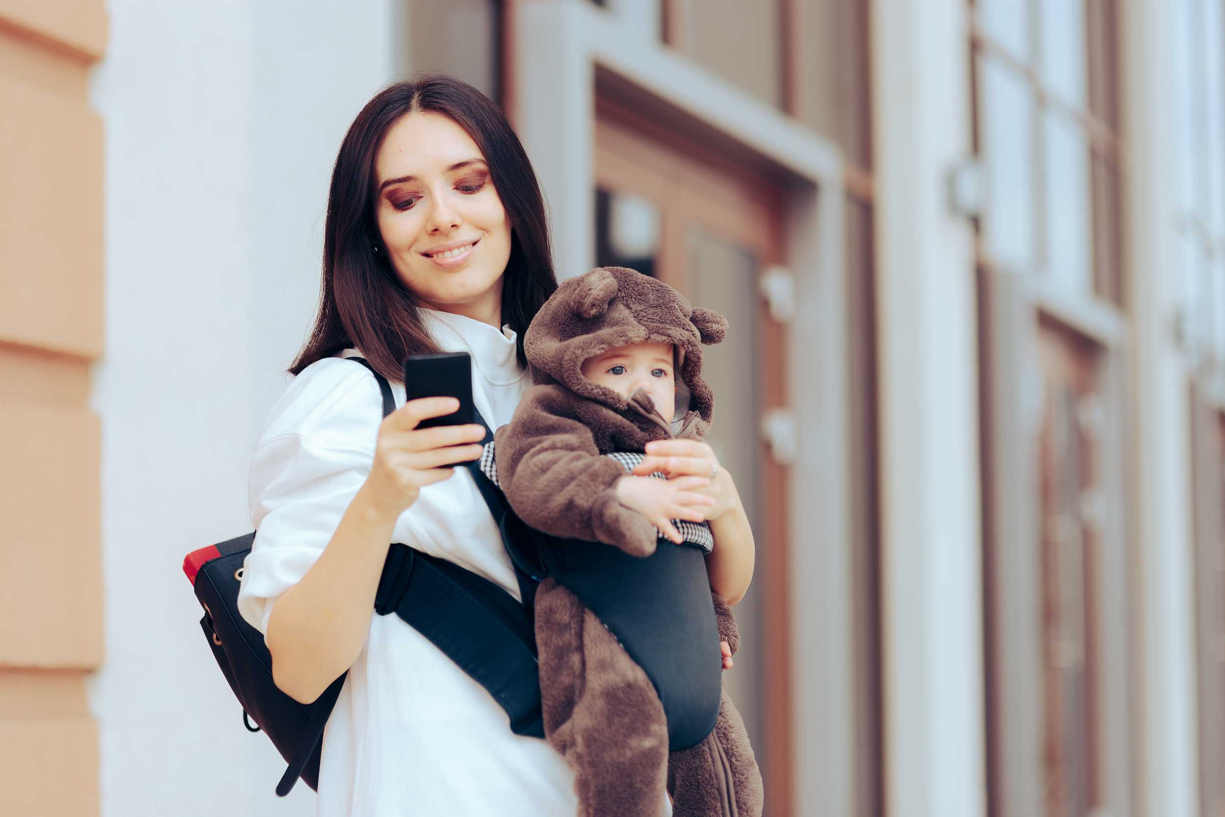 a mother carrying her baby and using her phone