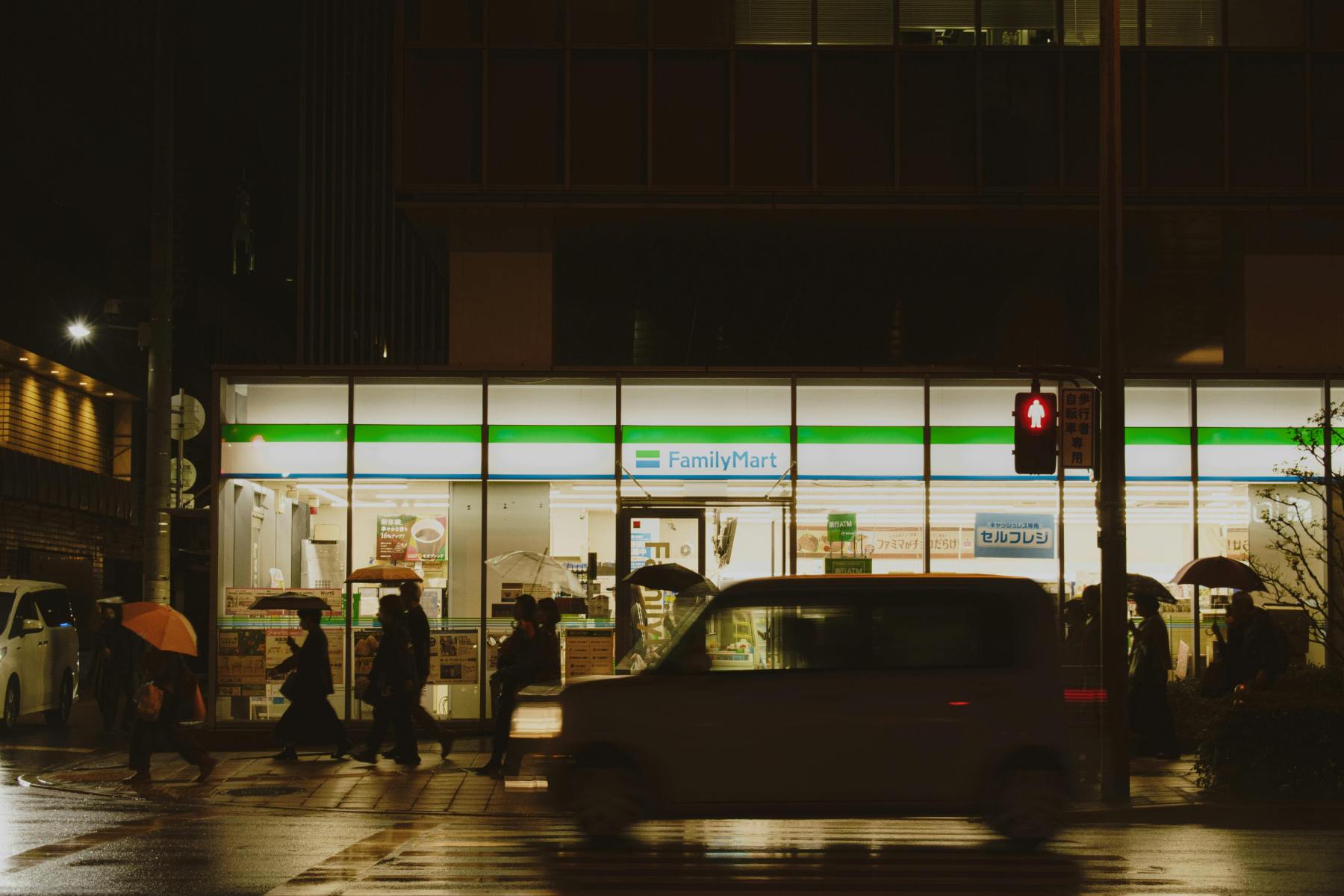Orang-orang menyeberang jalan dekat FamilyMart di Jepang saat malam hujan. Via Pexels (by Maxine Xin)