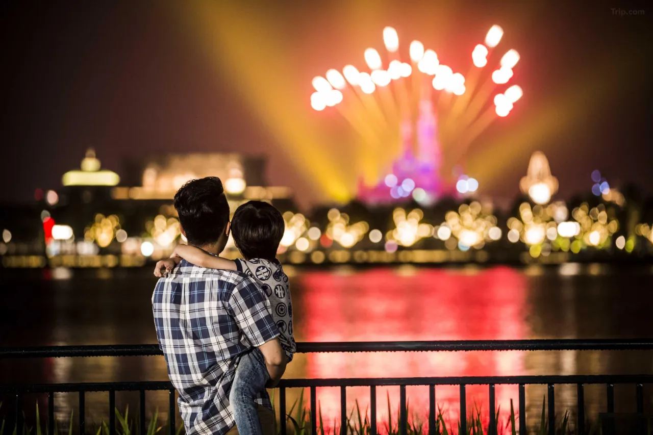 上海ディズニーランドの花火を眺める親子。ライトアップされたお城と湖面の反射が美しく輝く夜景。