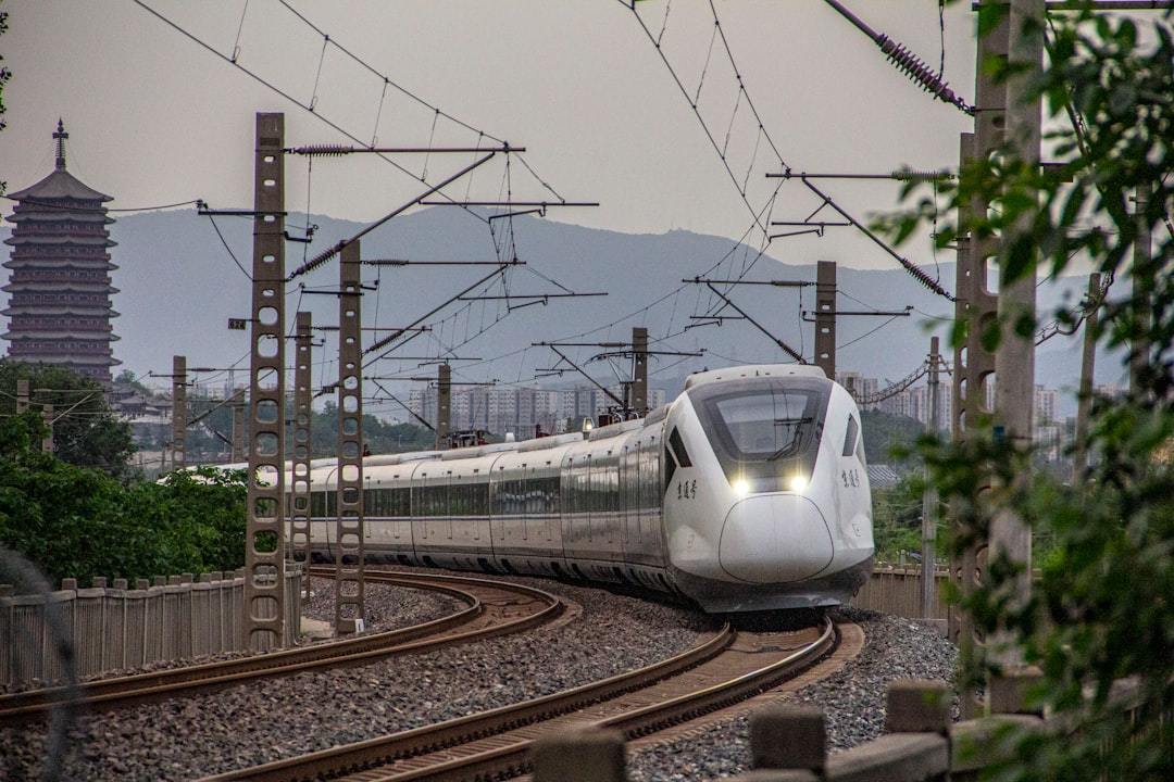 a white train traveling down train tracks next to a forest Via Unsplash (by logojackmowo Yao)