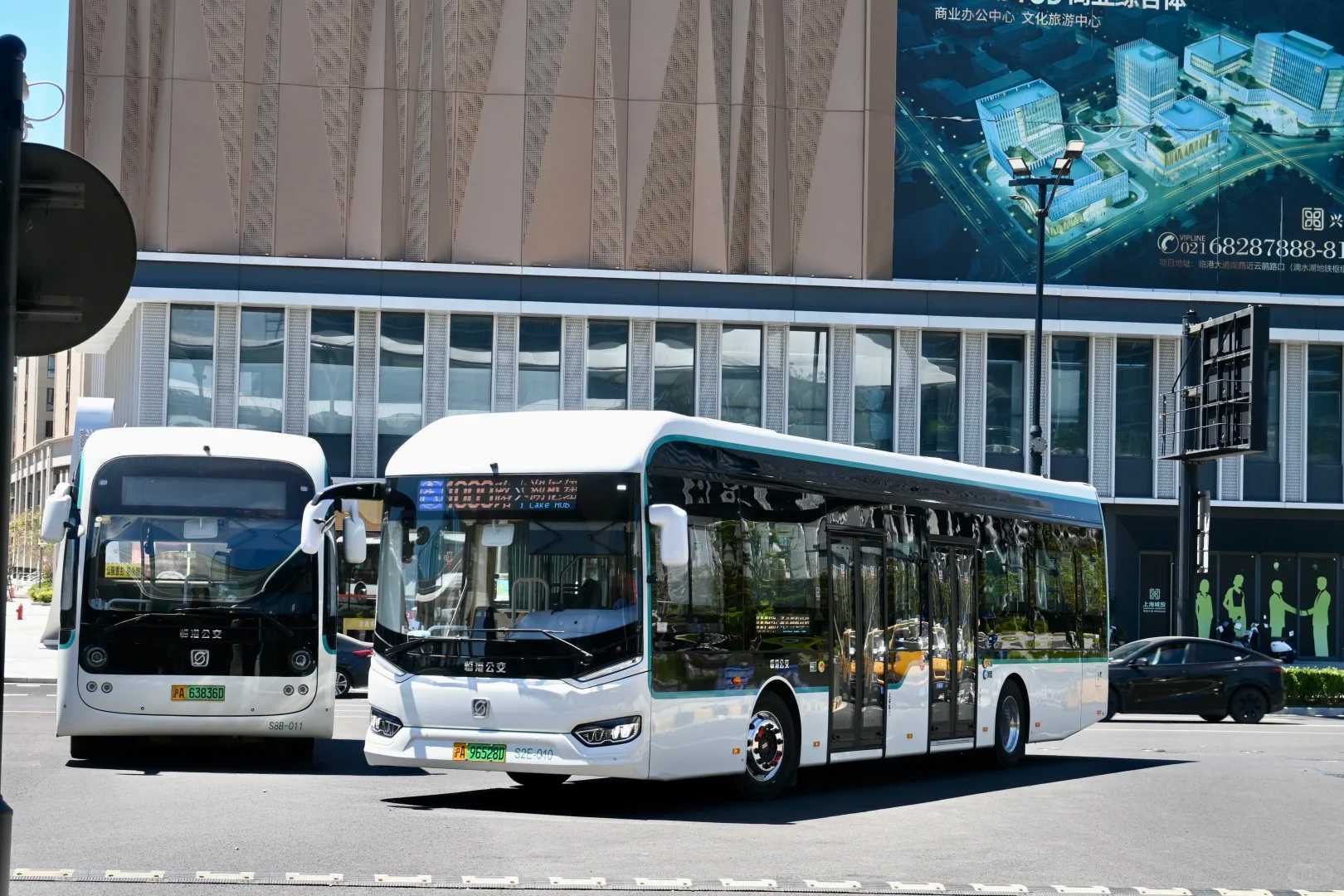 上海の街を走る白い電動バス。大型の近代建築を背景に、環境に優しい公共交通機関として運行されている様子。