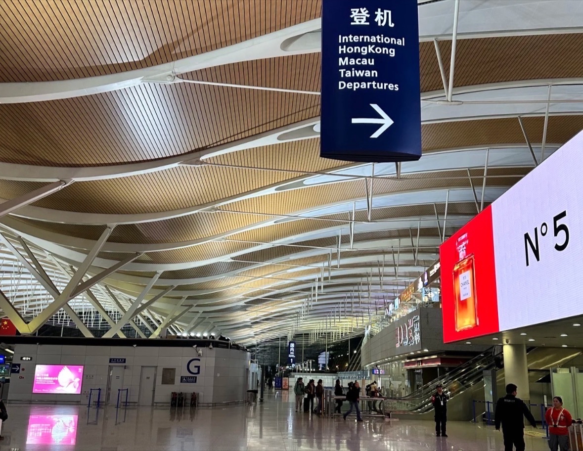 上海浦東国際空港の出発ロビー。国際線および香港・マカオ・台湾行きの搭乗口方向を示す案内板があり、明るく広々とした空港の内部が見える。