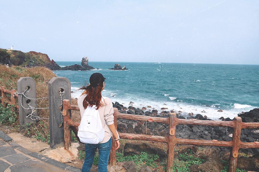 woman in white long sleeve shirt and blue denim jeans standing on brown wooden fence near near near near near Via Unsplash (by Yamin Ohmar)