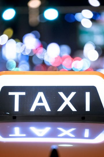 a close up of a taxi sign with blurry lights in the background Via Unsplash (by Janis Rozenfelds)
