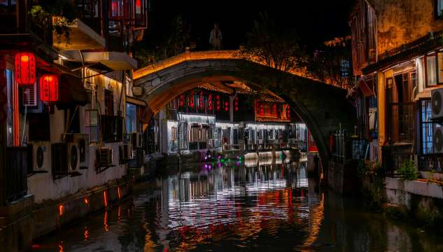 Canal iluminado de noche en Zhujiajiao con puente de piedra arqueado y faroles rojos reflejados en el agua