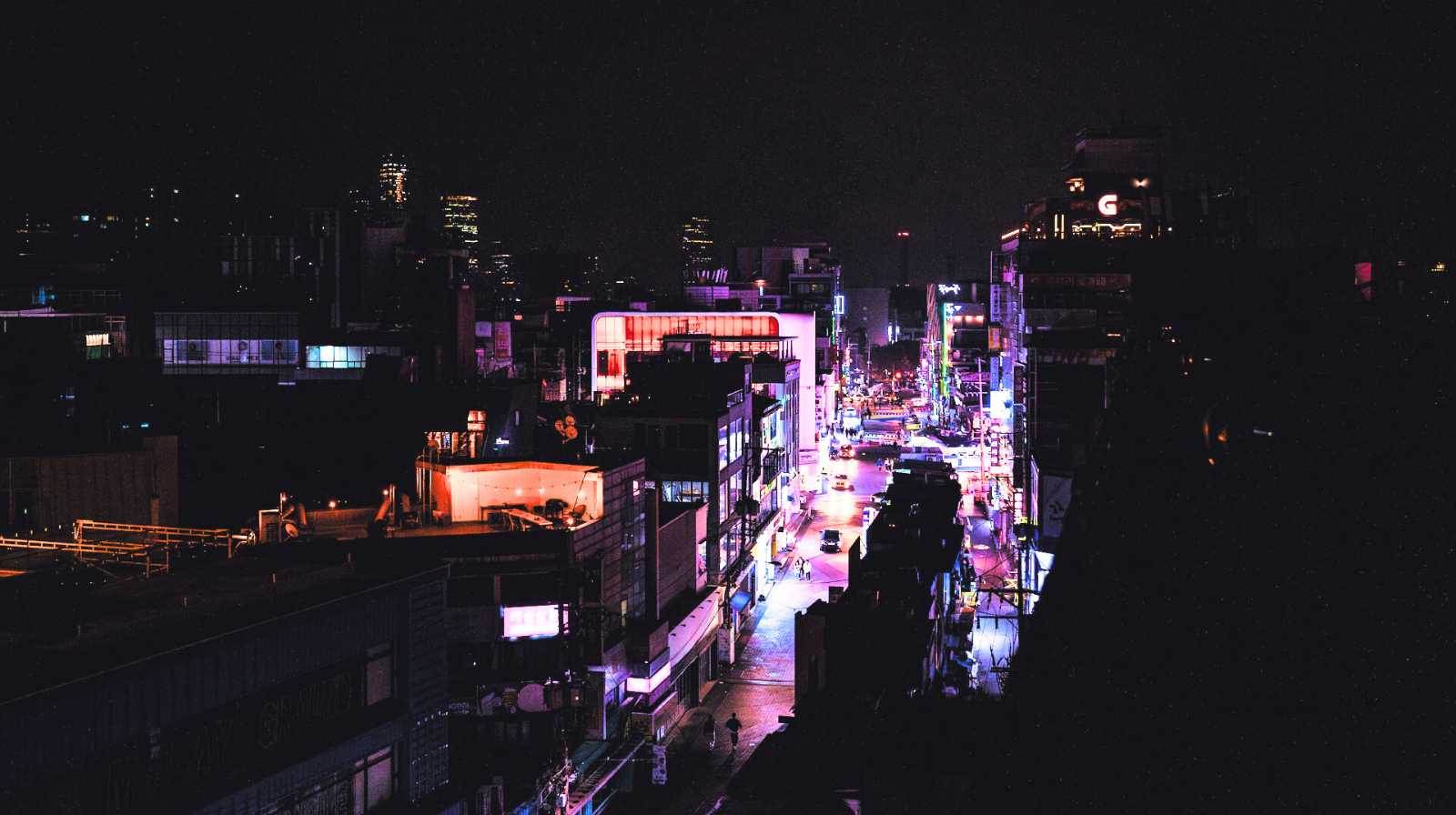 Vista nocturna de una calle de Seúl iluminada con luces neón y edificios modernos, con ambiente urbano y juvenil.