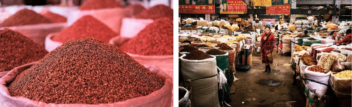 Mucchi di spezie essiccate in sacchi accanto a una donna che percorre i corridoi del mercato, con bancarelle di funghi e frutta secca sullo sfondo