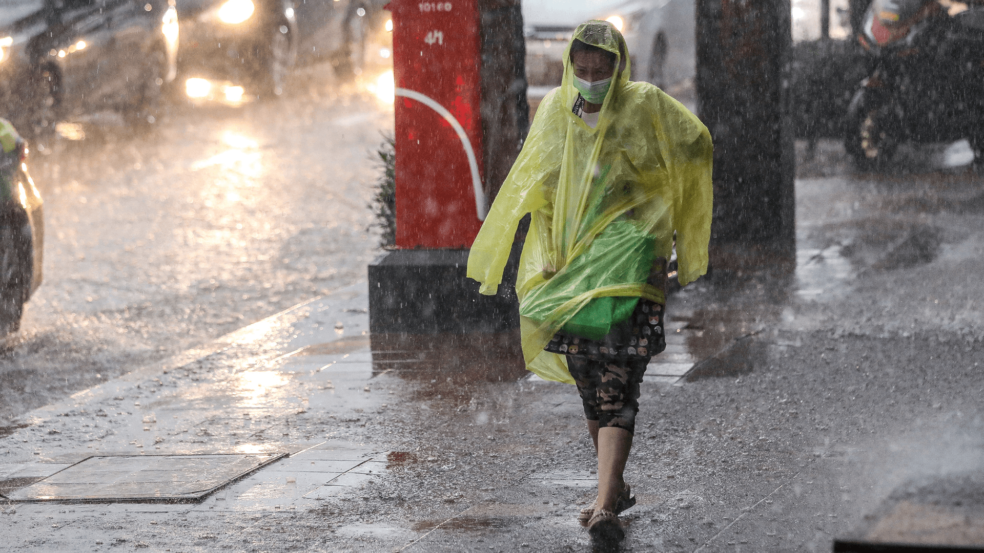 Person in a poncho, walking along a rainy busy road