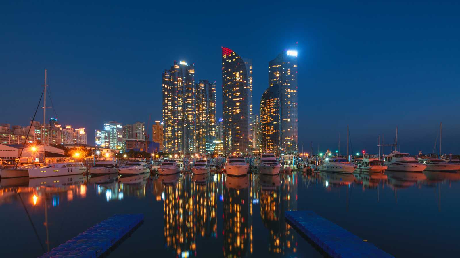 Puerto deportivo de Haeundae en Busan con yates y rascacielos iluminados reflejados en el agua