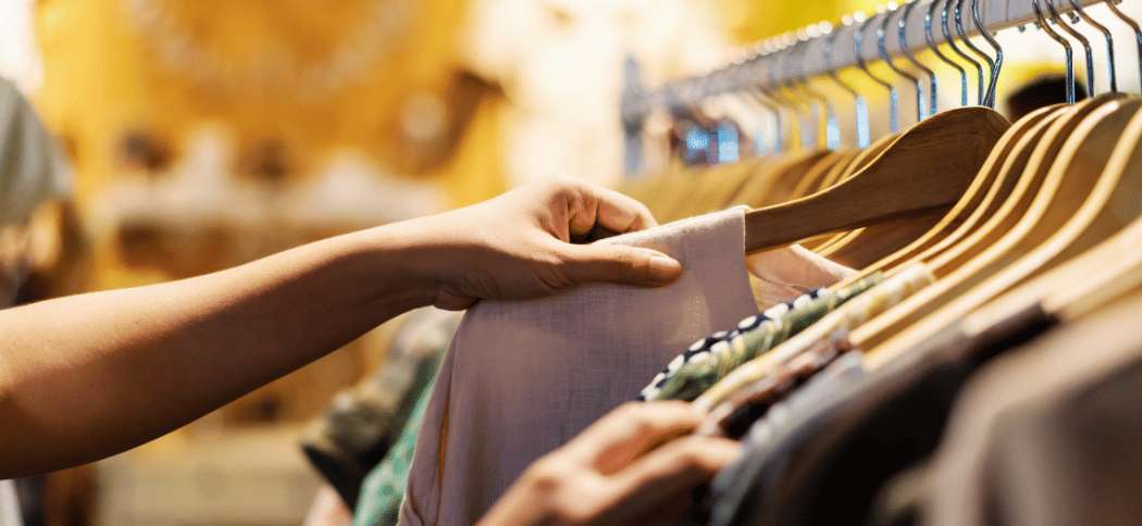 Persona revisando ropa colgada en un perchero de una tienda, ilustrando las opciones de compras