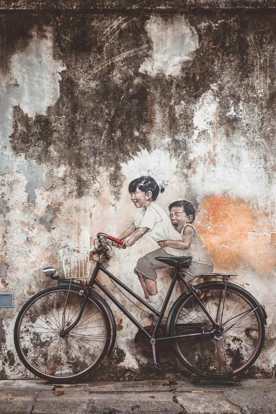 the famous street painting in penang of a little girl and her brother riding a bicycle