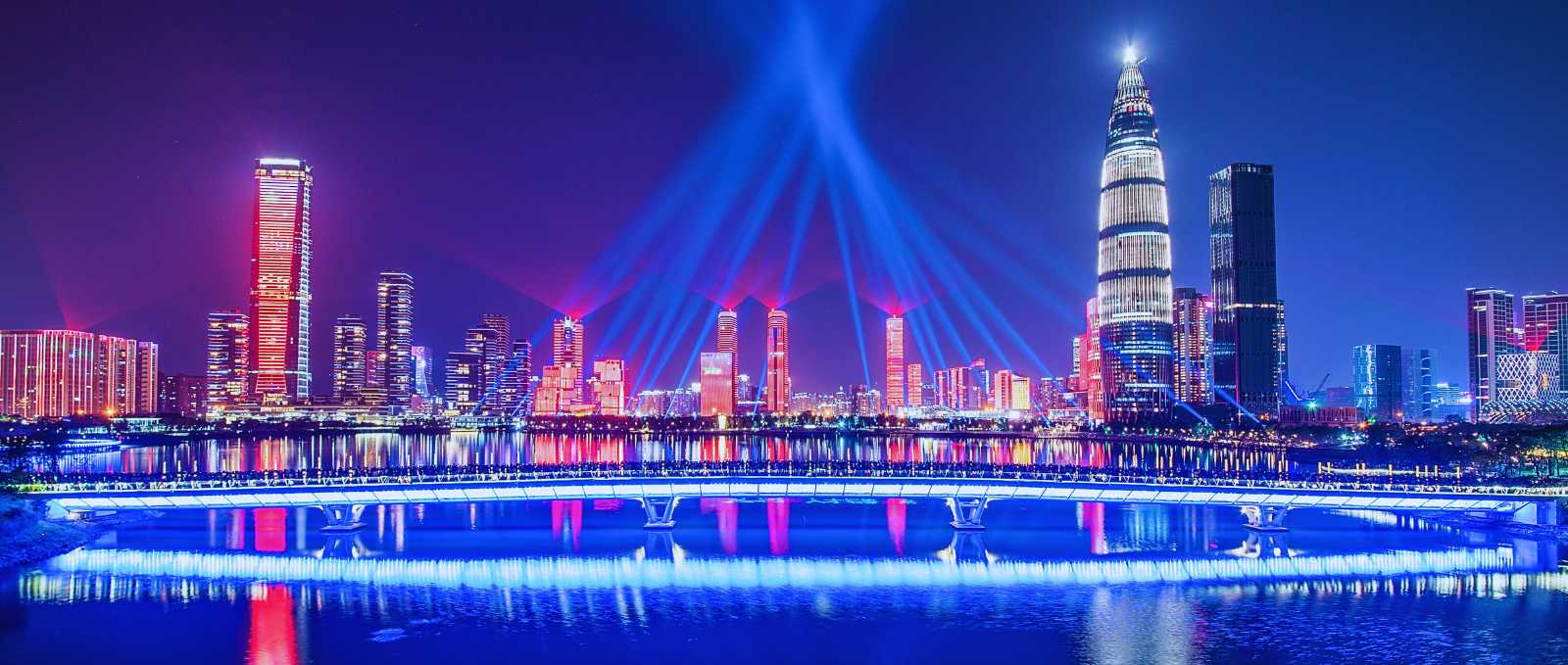 Shenzhen Bay by night, with illuminated skyscrapers, beams of light, and a modern bridge over the water