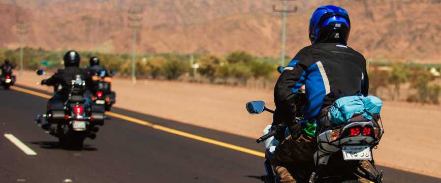 Grupo de motoristas viajando por una carretera en Marruecos con paisaje desértico al fondo