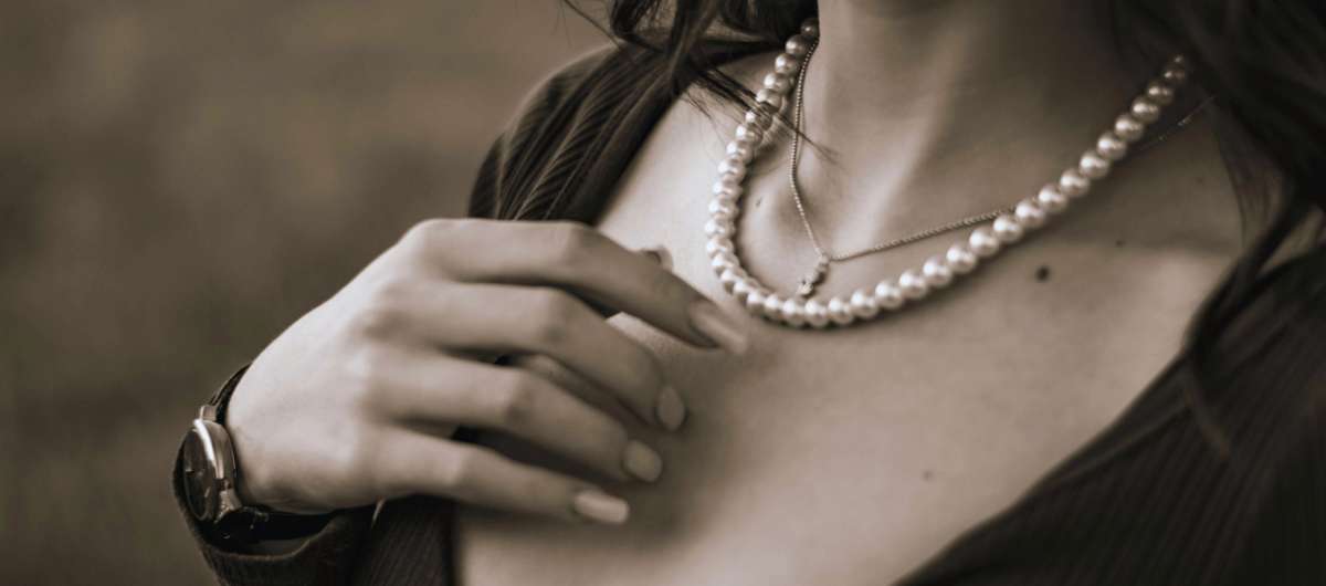 Mujer luciendo un collar de perlas naturales sobre el pecho, con la mano apoyada sobre el hombro