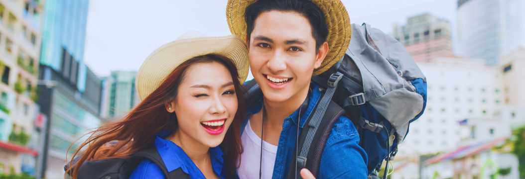 Pareja de turistas jóvenes con mochilas sonriendo en ciudad moderna, viaje en pareja y turismo urbano.