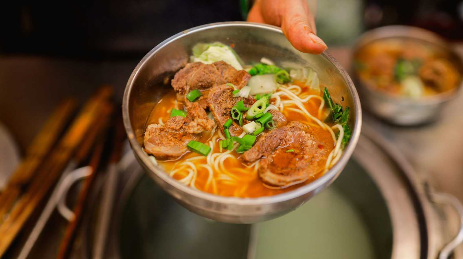 Cuenco de beef noodle soup taiwanés con fideos, caldo rojo, trozos de carne y cebollín fresco, servido recién hecho