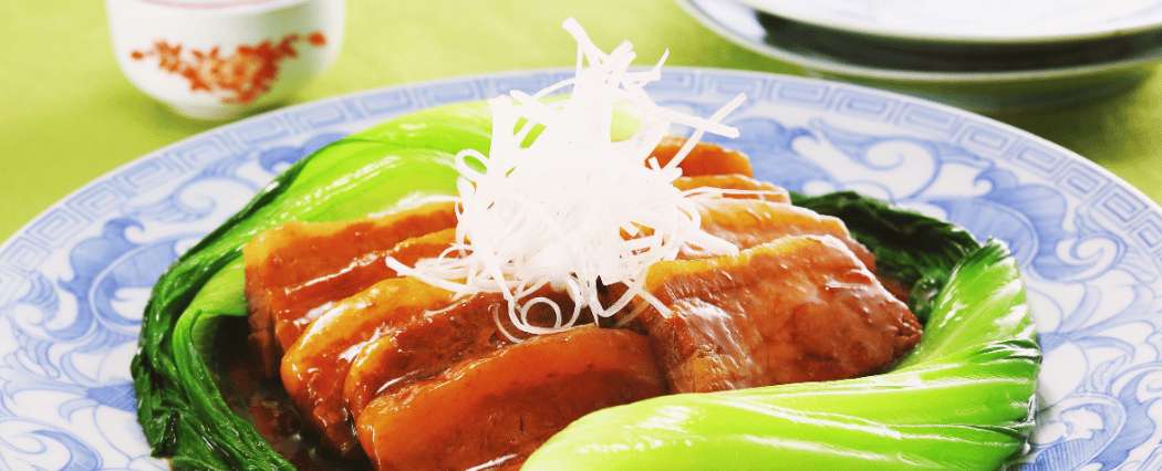 Panceta de cerdo estilo Dongpo (hong shao rou) sobre bok choy, acompañada de rábano en juliana, en un plato tradicional chino