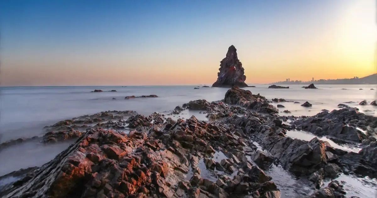 Playa de Shilaoren en Qingdao con formaciones rocosas junto al mar al atardecer.