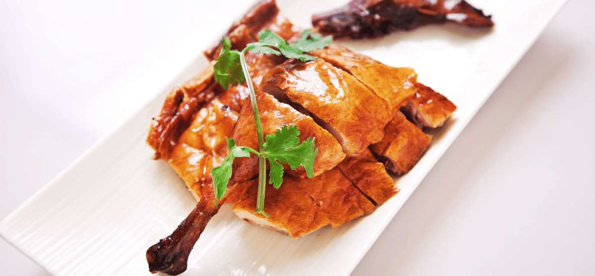 Pato asado al estilo cantonés cortado en trozos y servido en un plato blanco, decorado con hojas de cilantro