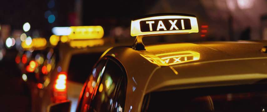 Taxi con señal iluminada circulando de noche en una ciudad asiática, transporte urbano para moverse durante una escala.