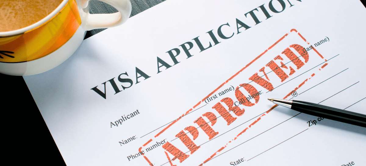 Approved visa application form with an "Approved" stamp on a desk with a pen