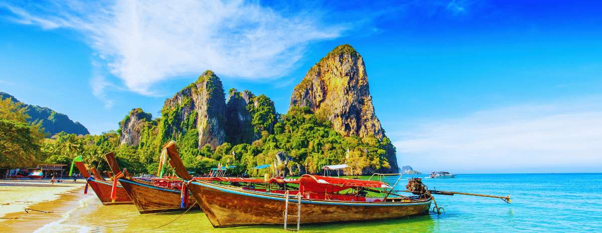 Traditional Thai long-tail boats on a tropical beach with karst mountains and turquoise sea in Krabi
