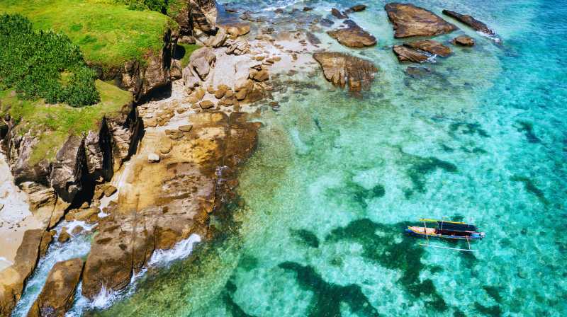 Costa rocosa de Lombok con acantilados verdes y una embarcación sobre aguas transparentes