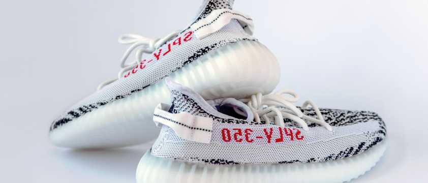 Zapatillas deportivas blancas con detalles negros y suela translúcida sobre fondo neutro