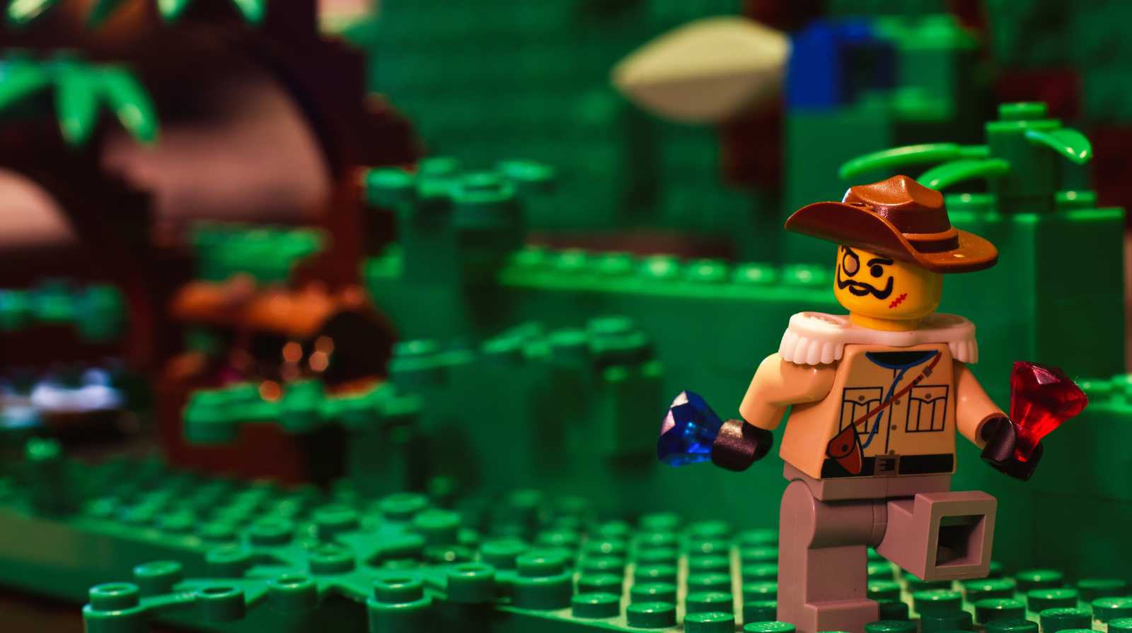 Figura de Lego con sombrero explorador sosteniendo dos gemas de colores en una escena de bosque hecho con piezas verdes
