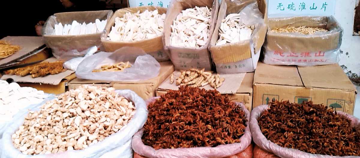 Scatole e sacchi con radici, cortecce e anice stellato essiccati in vendita in una bancarella di un mercato cinese