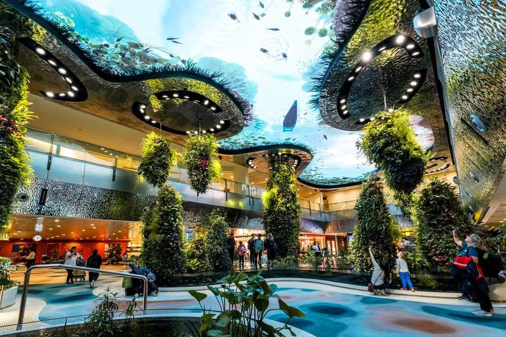 Visitors walking through the lush indoor gardens beneath the ocean-themed digital ceiling at Changi Airport