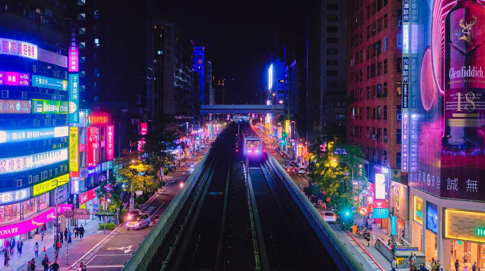Tren del MRT de Taipéi circulando por una línea elevada entre luces de neón y edificios nocturnos