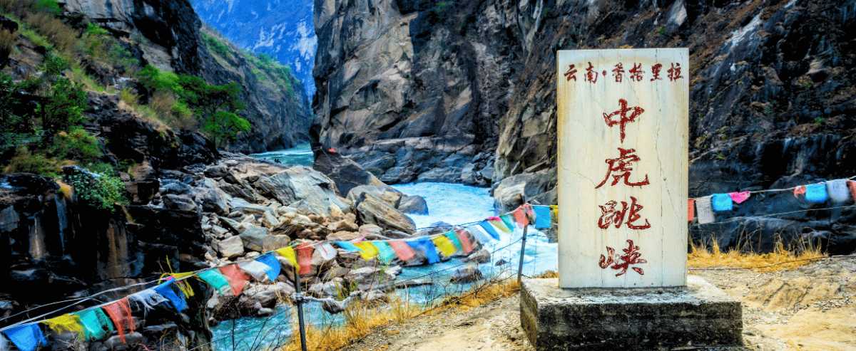 Cartello della Gola del Salto della Tigre lungo il fiume Jinsha, tra canyon rocciosi nello Yunnan.