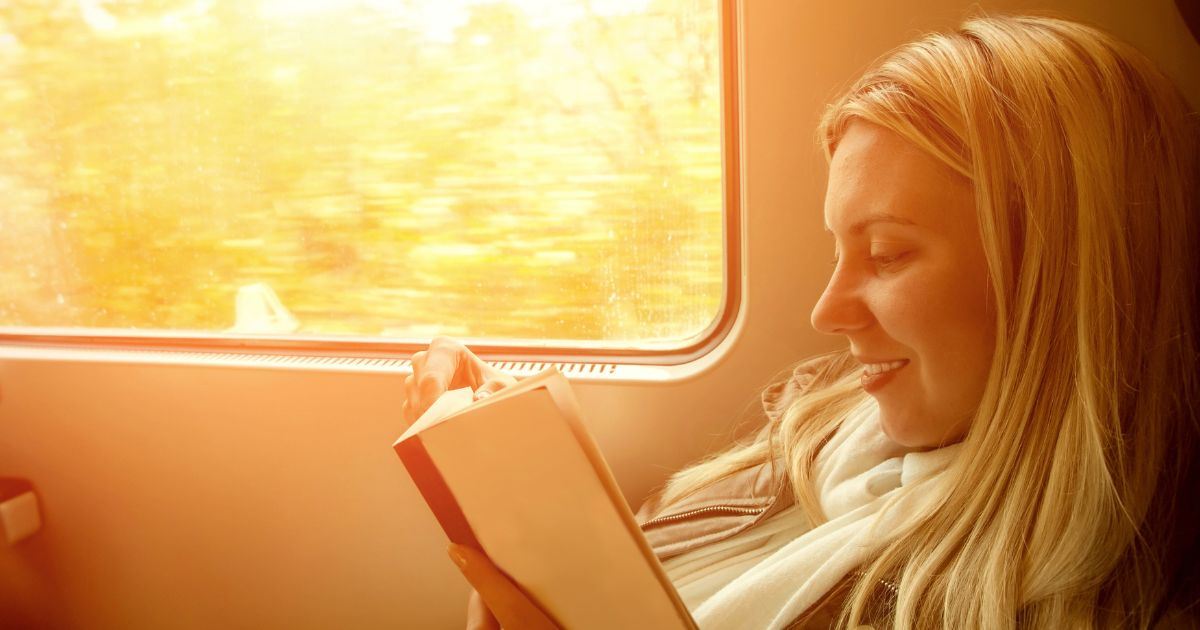 A woman reading a book while sitting on a window seat of the train