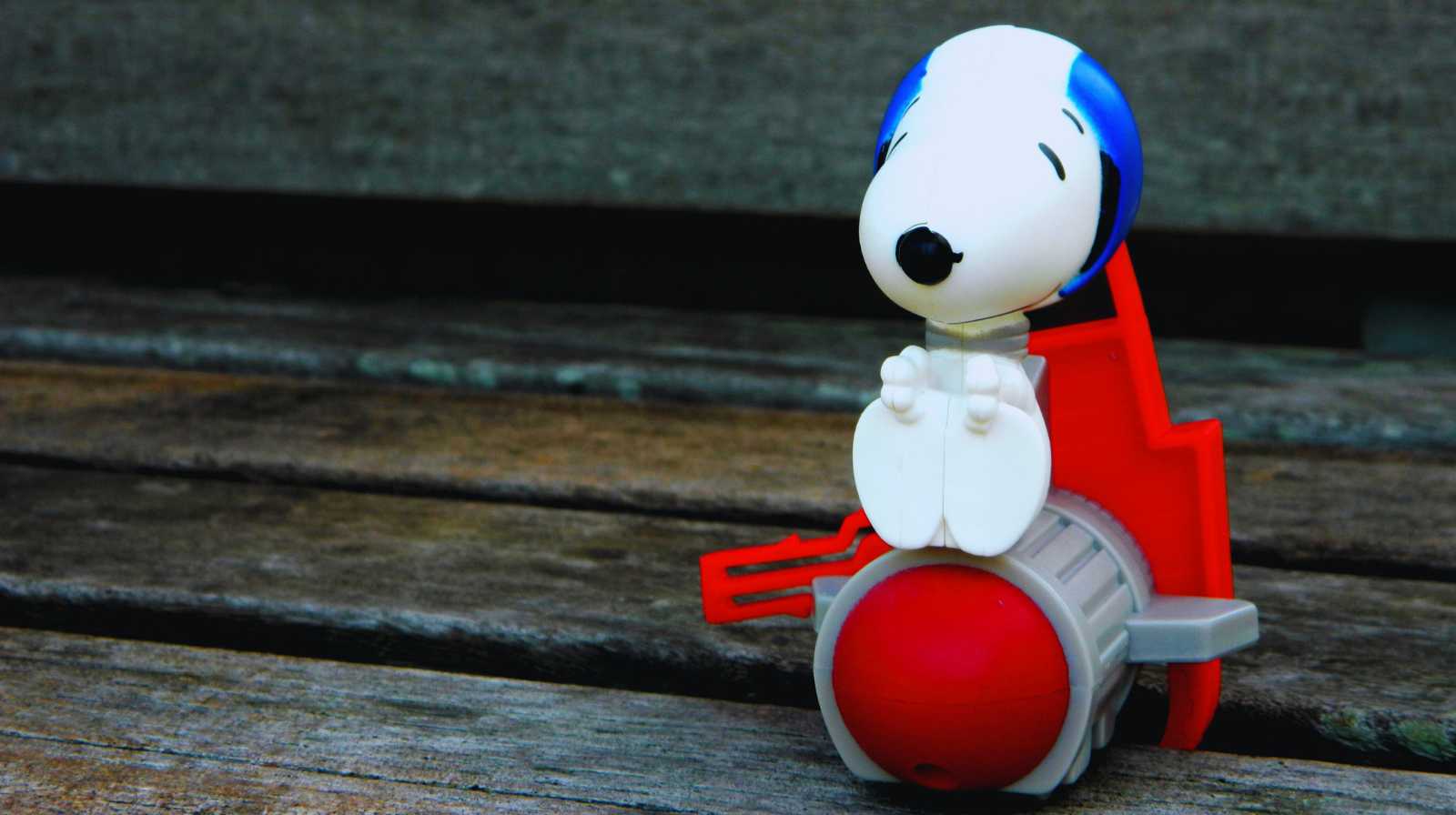 Figura de Snoopy sentada sobre un pequeño cohete rojo colocada en un banco de madera envejecido