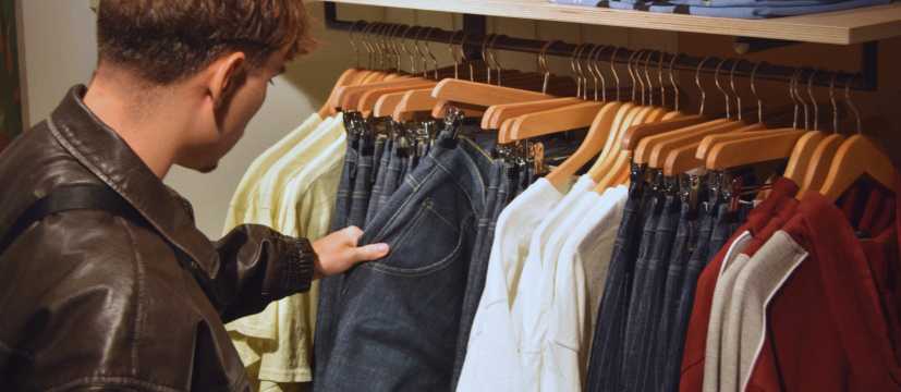Hombre revisando jeans en una tienda de ropa con perchas de madera