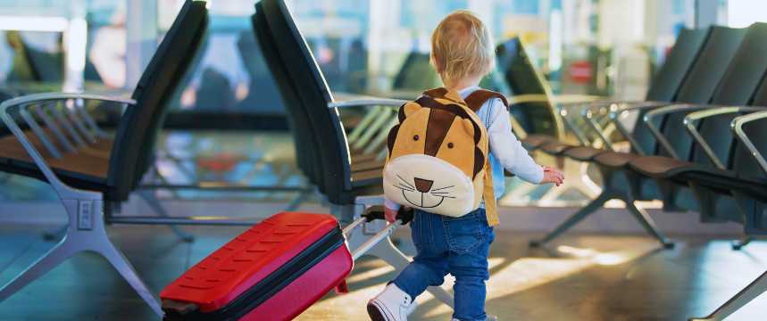 Niño pequeño caminando por un aeropuerto con una maleta roja y una mochila infantil, escena de viaje en familia
