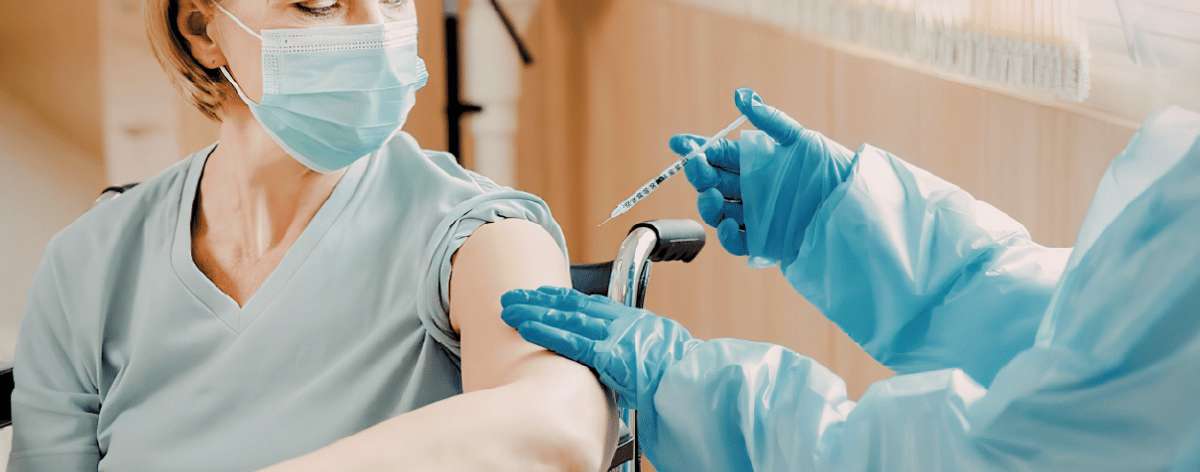 Une personne recevant un vaccin, entourée de personnel soignant portant un équipement de protection.